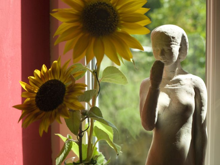 Scultura semplice in un ambiente luminoso, circondata da girasoli che portano un tocco di colore.