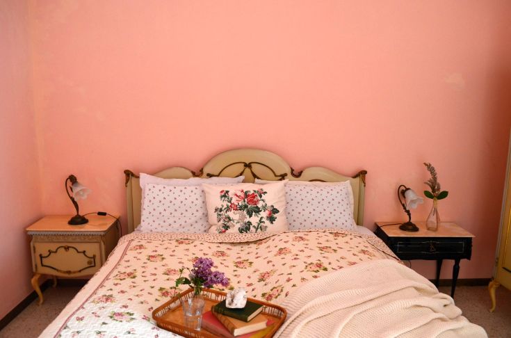 Camera semplice con parete rosa, letto ben curato e decorazioni sobrie. Un luogo tranquillo per riposare.