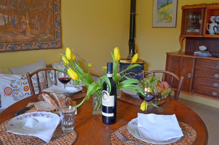 Una tavola apparecchiata con vino, pane e fiori, in un ambiente rustico e confortevole.