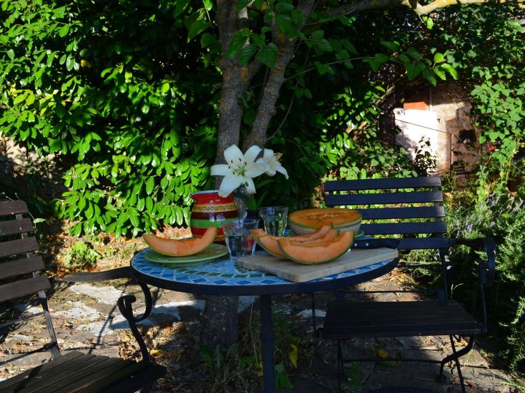 Un tavolo all'aperto con meloni e fiori circondato da un ambiente tranquillo e verdeggiante.