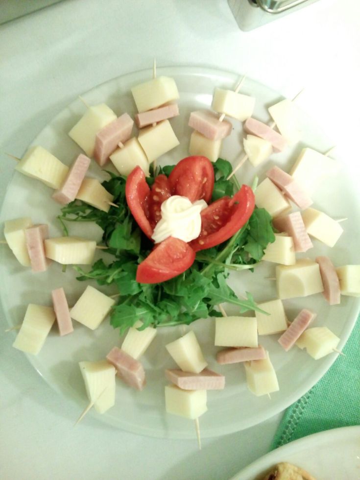 Selezione di spiedini di formaggio e prosciutto serviti su un letto di rucola e pomodorini.