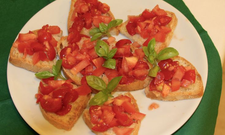Bruschette condite con pomodoro fresco e foglie di basilico, un antipasto semplice e saporito.