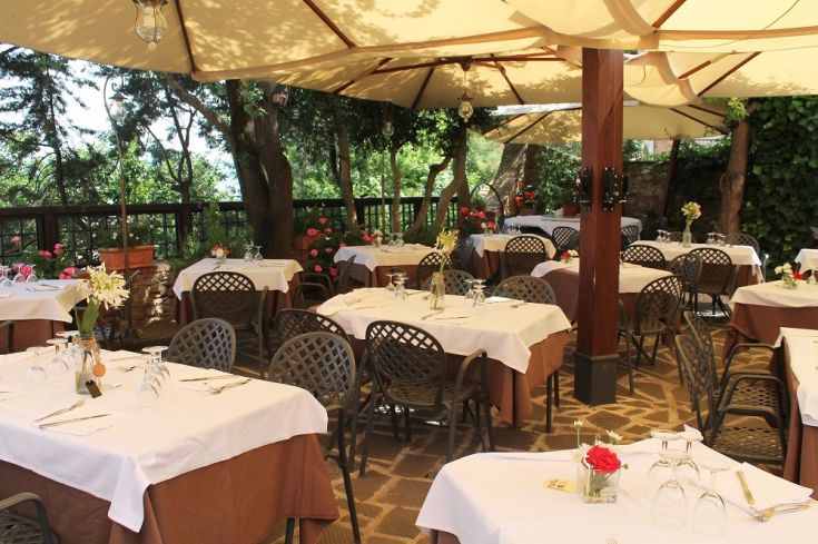 Restaurant en plein air avec des tables en bois, entouré de verdure et de fleurs, idéal pour des dîners intimes.