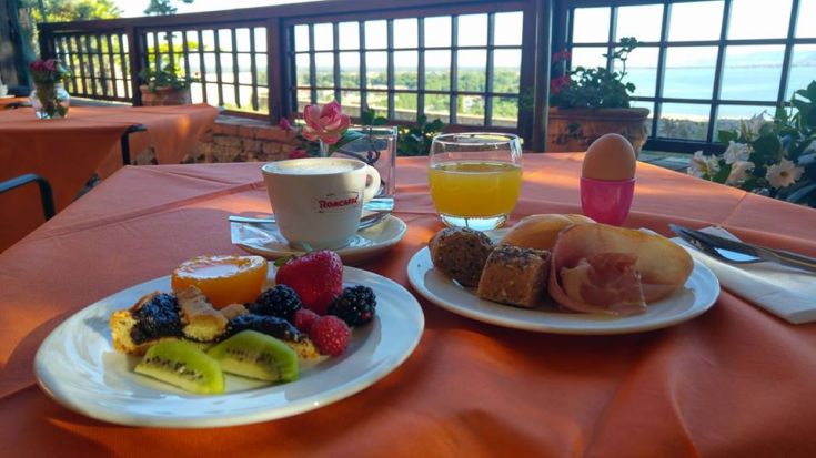 Petit déjeuner avec des fruits frais, des pâtisseries et des boissons, proposé dans un cadre avec vue sur le lac.