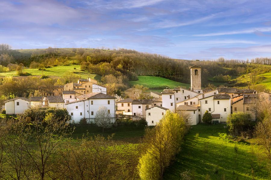 A small village with light-colored houses set in a green hilly landscape under a clear sky.