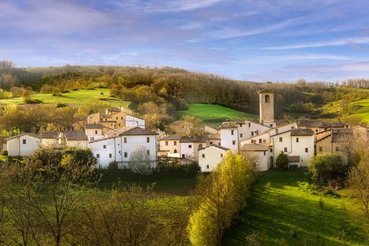 Ein kleines Dorf mit hellen Häusern in einer grünen Hügellandschaft unter einem klaren Himmel.