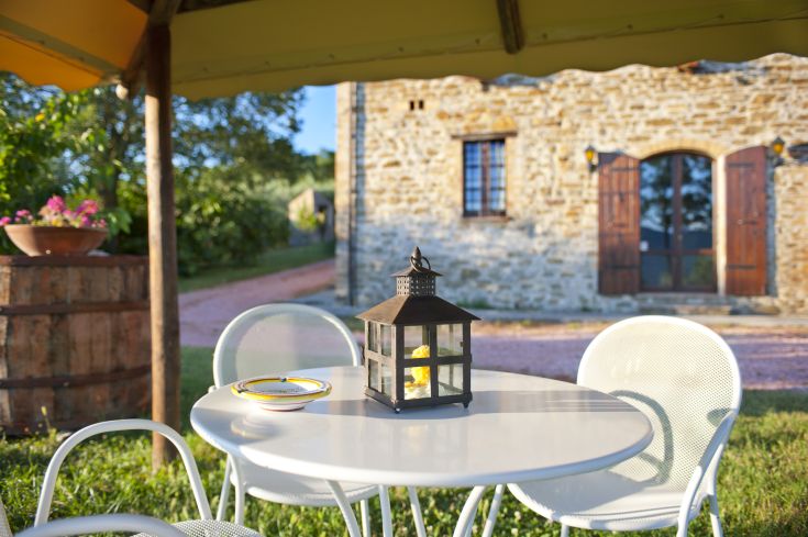 Une simple table de jardin avec une lanterne, entourée par un panorama sur une vieille ferme.