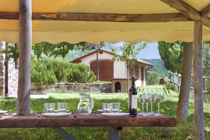 Une table extérieure avec un grand parapluie, prête pour un déjeuner avec des plats et du vin.