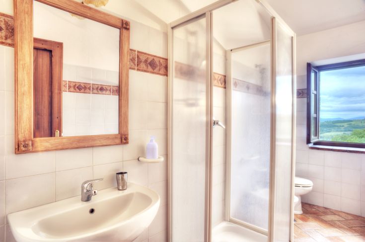 Salle de bain lumineuse avec une fenêtre éclairant l'espace, équipée d'une douche et d'un lavabo simples.