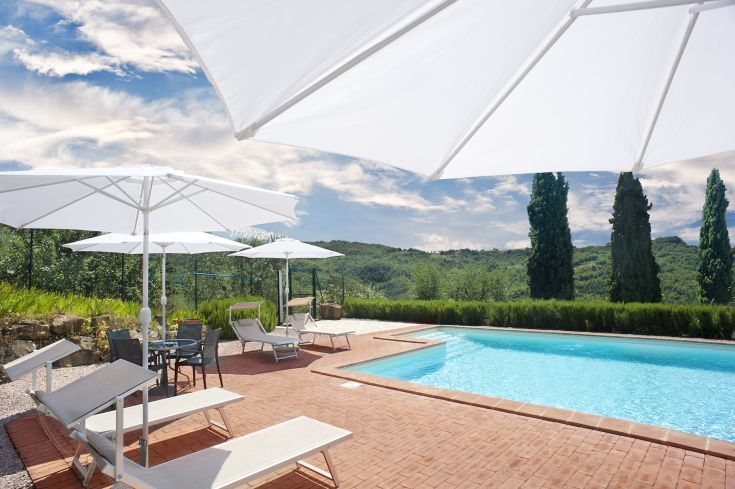 Une piscine avec des chaises longues et des parasols, entourée de collines sous un ciel dégagé.