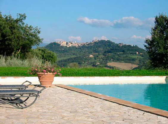 Panorama della campagna umbra con una piscina in primo piano e una collina sullo sfondo.