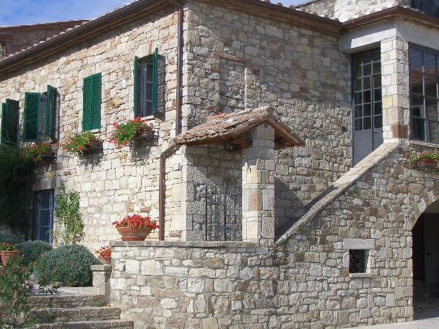 Un edificio in pietra con finestre verdi circondato da piante e fiori, immerso nel paesaggio naturale.