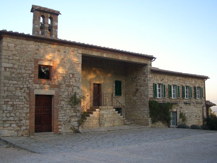 Tipica villa umbra con facciata in pietra e finestre verdi, immersa nella natura.