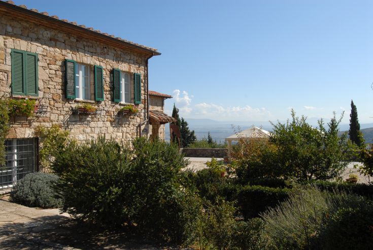 Scena di un agriturismo in un paesaggio tranquillo, con un giardino ben tenuto e un cielo limpido.