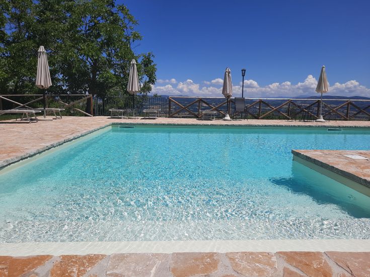 Piscina blu circondata da un'area verde, con ombrelloni a disposizione per il relax.