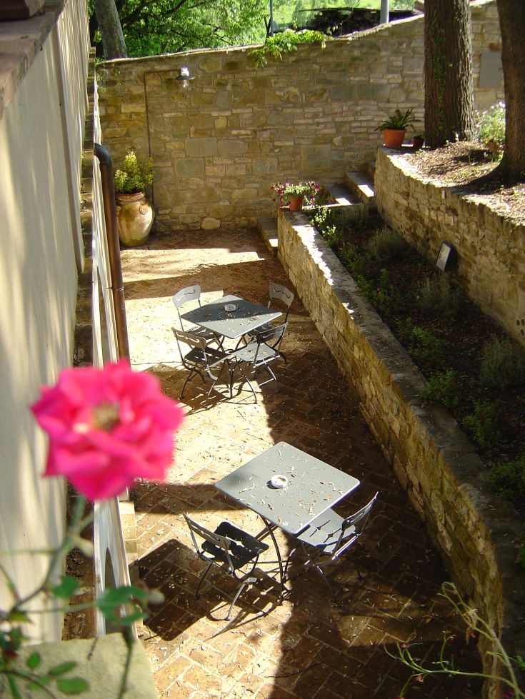 Ein heller Innenhof mit metallischen Tischen, umgeben von grünen Pflanzen und einer hervorgehobenen Rose.