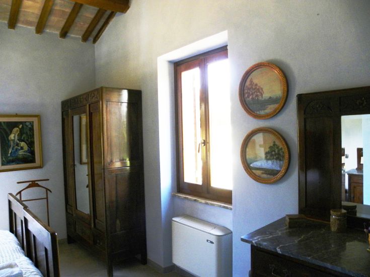 Bright room furnished with wooden furniture, overlooking a gentle green hill.