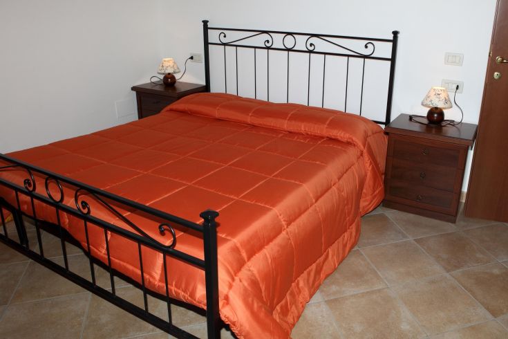 Spazio accogliente con letto matrimoniale e biancheria dai toni arancioni, perfetto per un soggiorno tranquillo.