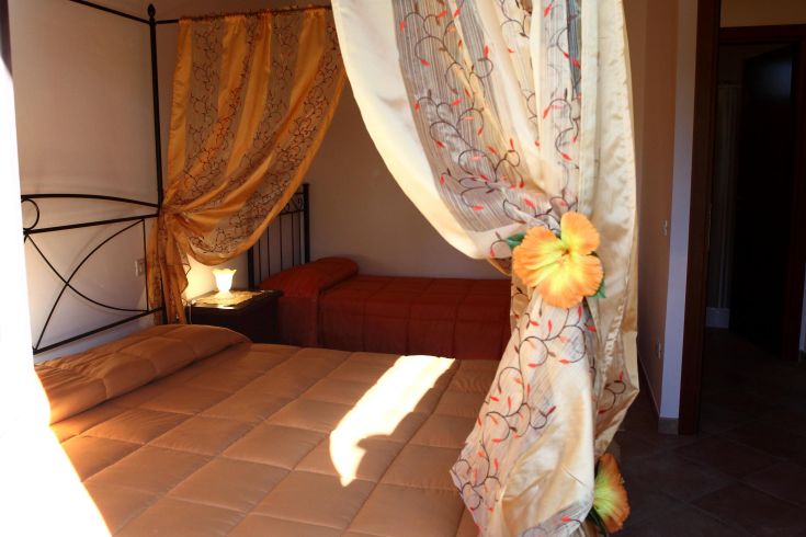 Una camera semplice con letti, tende leggere e buona illuminazione naturale.