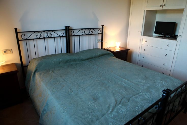 Camera luminosa con letto matrimoniale, dotata di arredamento essenziale e decorazioni sobrie.