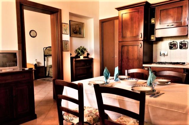 A simple living room with a set dining table, furnished in wood and illuminated by natural light.