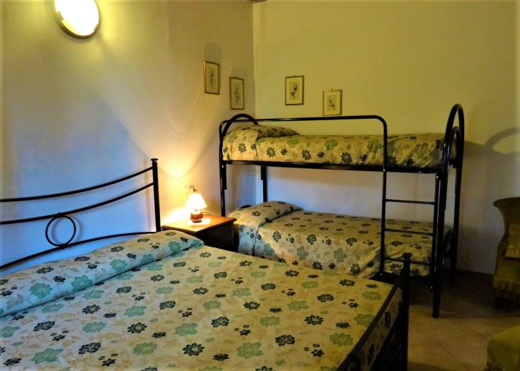 Simple room with bunk beds and a double bed, illuminated by a warm-toned lamp.