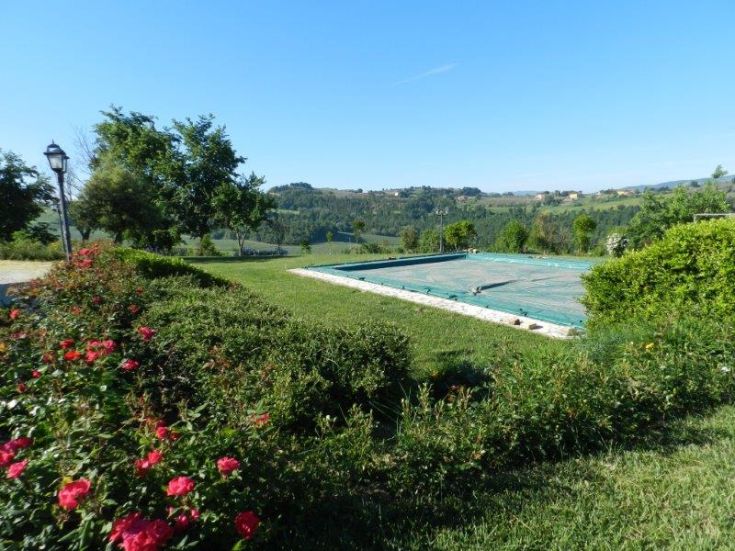 Szene eines Agriturismo mit einem Pool, umgeben von Bäumen und typischen grünen Flächen Umbriens.