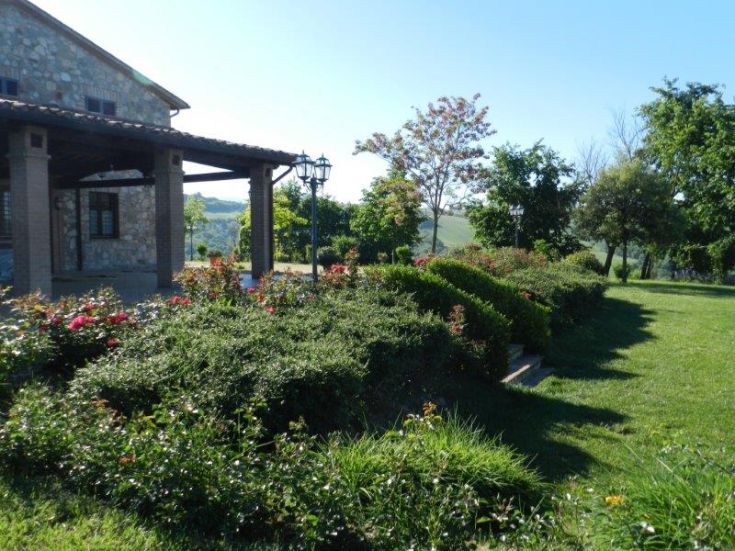 Eine Szene eines Bauernhofs, umgeben von der Natur, mit gepflegten Gärten und blühenden Pflanzen.