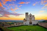 La Basilica di San Francesco d'Assisi al tramonto, circondata da un suggestivo paesaggio collinare.
