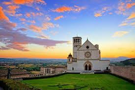 La Basilica di San Francesco d'Assisi al tramonto, circondata da un suggestivo paesaggio collinare.