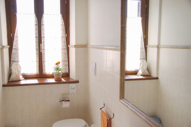 Spacious, bright bathroom with a window for natural light; adorned with a simple flower and a fabric bag.