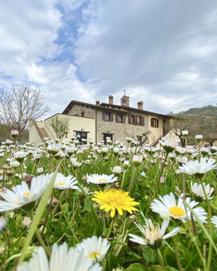 A renovated building surrounded by a garden with colorful flowers, ideal for stays in Umbria.