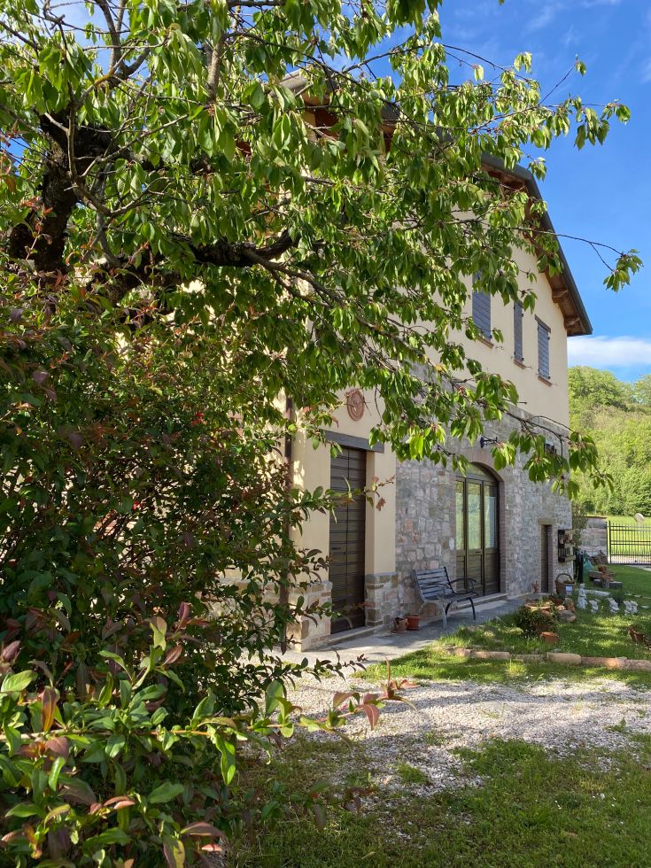 A country house surrounded by lush Umbrian greenery, featuring a garden and parking areas.