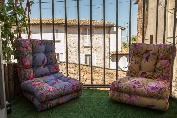 Two floral decorated armchairs on the balcony of a historic building.