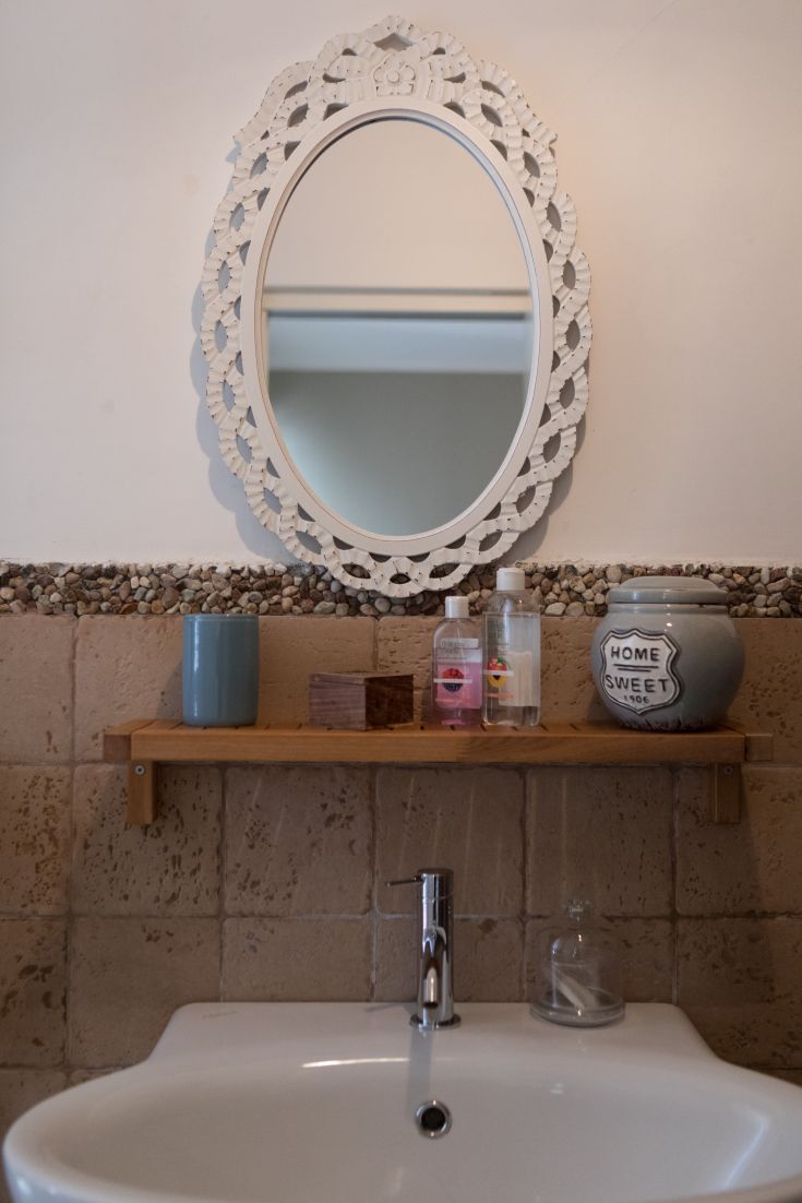 A simple bathroom with a framed mirror and a wooden shelf, ideal for relaxing moments.