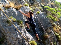 Un'arrampicatrice scala una roccia in un ambiente naturale, dimostrando abilità e determinazione.