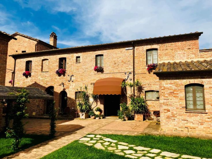 Ferme caractérisée par des murs en briques et des fleurs, entourée d'une végétation luxuriante. Une ambiance sereine et accueillante à la campagne.