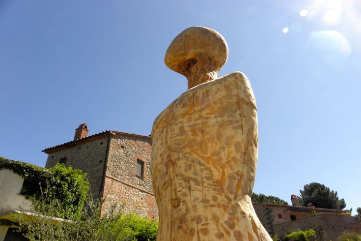 Eine Holzskulptur befindet sich in einer ländlichen Umgebung unter einem ruhigen Himmel.