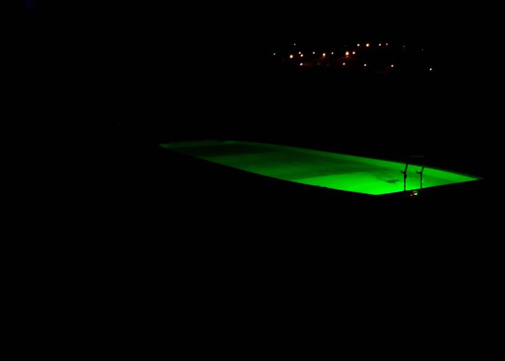 Ein grün beleuchteter Pool, der nachts eine friedliche Atmosphäre schafft.