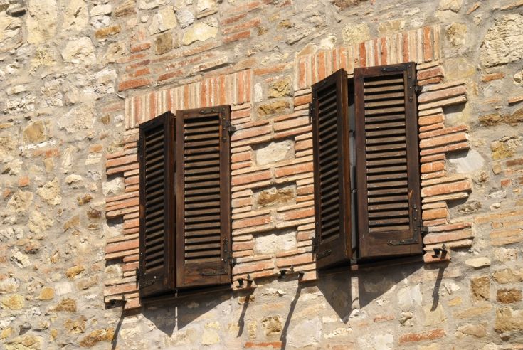 Two wooden windows of a building on a stone wall with bricks.
