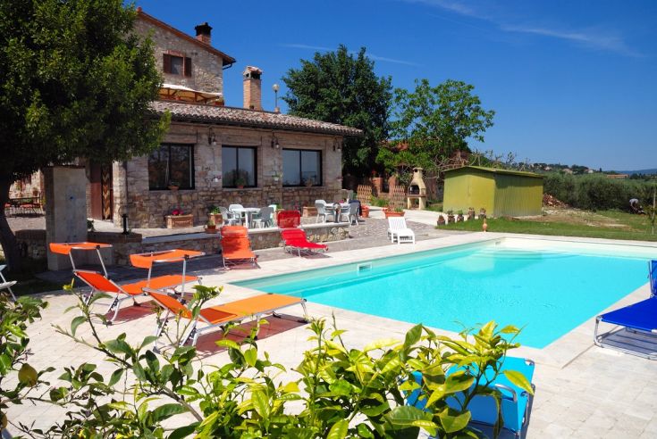 A historical farmhouse with a garden, featuring a pool and a stone building surrounded by greenery.