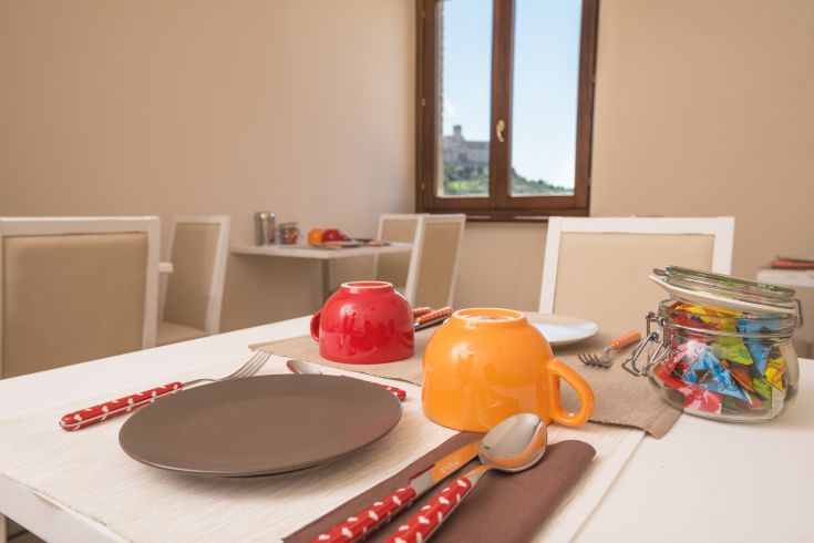 Tavola apparecchiata con stoviglie colorate in un ambiente accogliente, con panorama sulla natura circostante, perfetta per una colazione tranquilla.