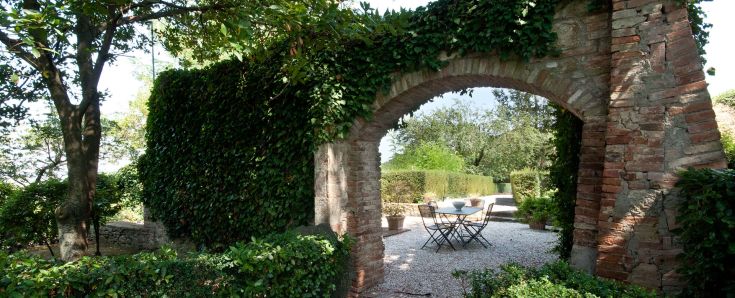 Un tranquillo angolo di giardino con un arco in mattoni e tavoli, perfetto per momenti di relax all'aperto.