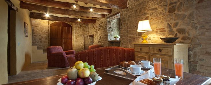 Una confortevole sala con pareti in pietra, illuminazione calda e un cesto di frutta fresca. Ambiente adatto per momenti di calma.