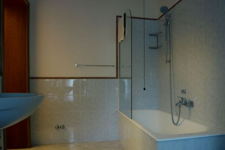 Salle de bain moderne avec baignoire et douche, carrelage clair, bien éclairée, ambiance chaleureuse.