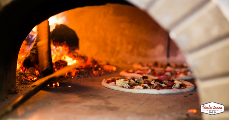 Pizza en train de cuire dans un four à bois, avec des flammes et une ambiance chaleureuse.