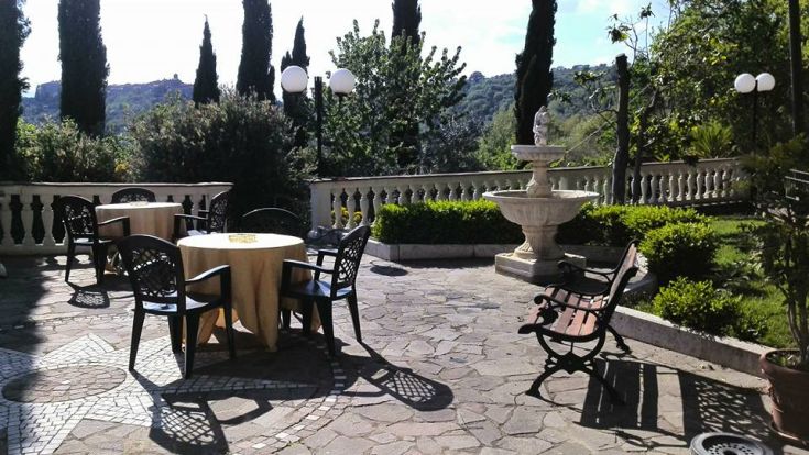 Une agréable zone extérieure avec des tables et des chaises, caractérisée par une fontaine et de vastes zones vertes.