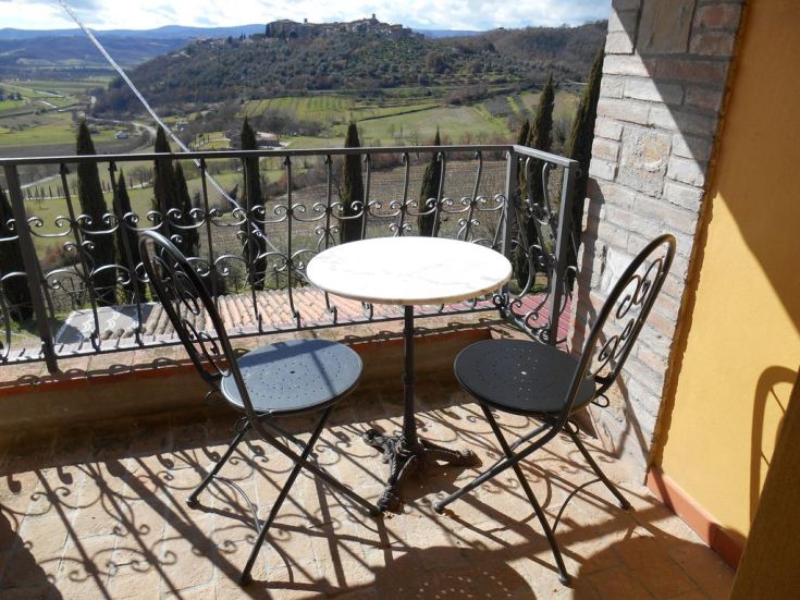 Table et chaises en fer forgé sur un balcon avec vue sur les douces collines de l'Ombrie.