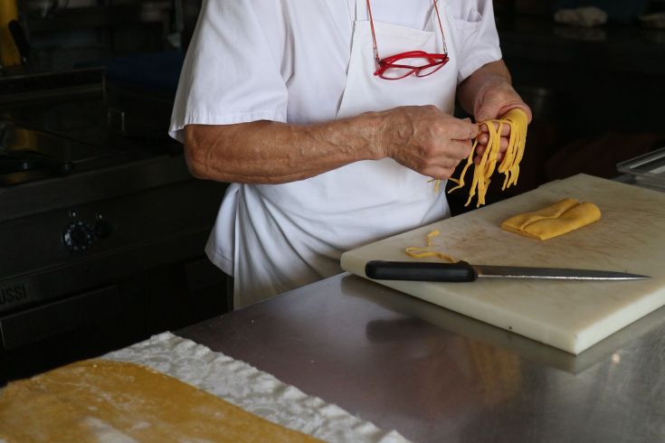 Un chef prépare des pâtes fraîches dans une cuisine simple et accueillante.
