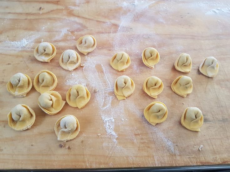 Tortellini frais faits maison, prêts à être cuisinés, disposés sur une table en bois.